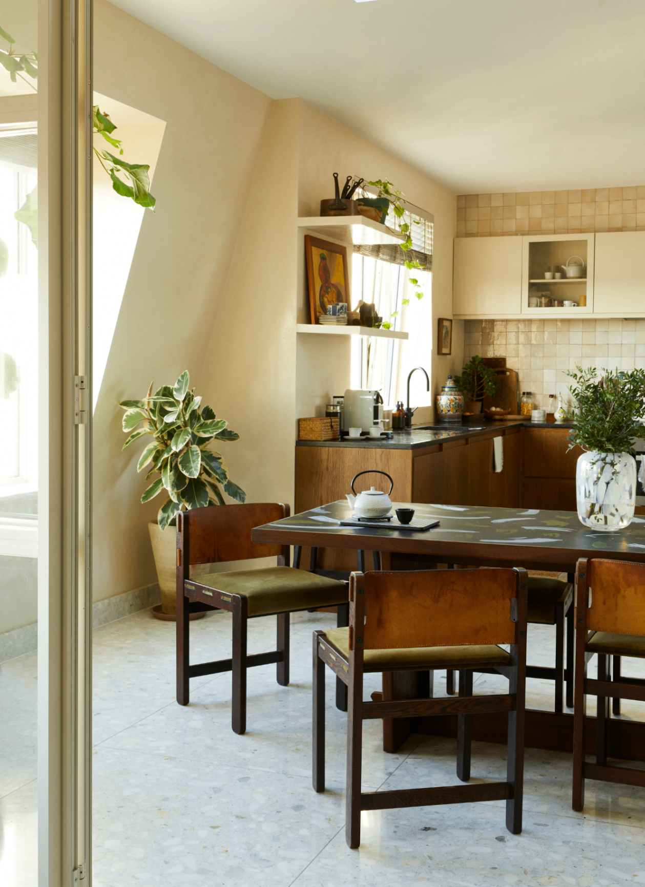 unlit open plan dining space with a wooden table, olive green upholstered chairs, terrazzo tile floor, and sloped ceiling skylight