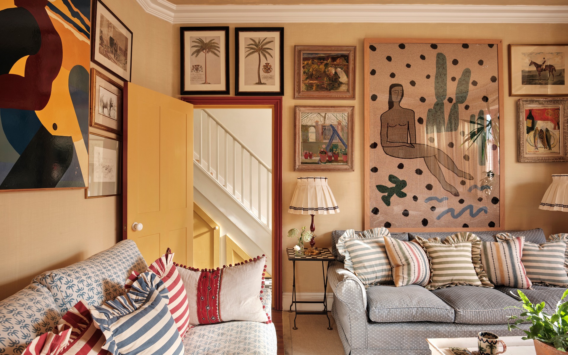 a living room with beige walls and lots of different sized artwork and a grey sofa with multicoloured candy stripe cushions
