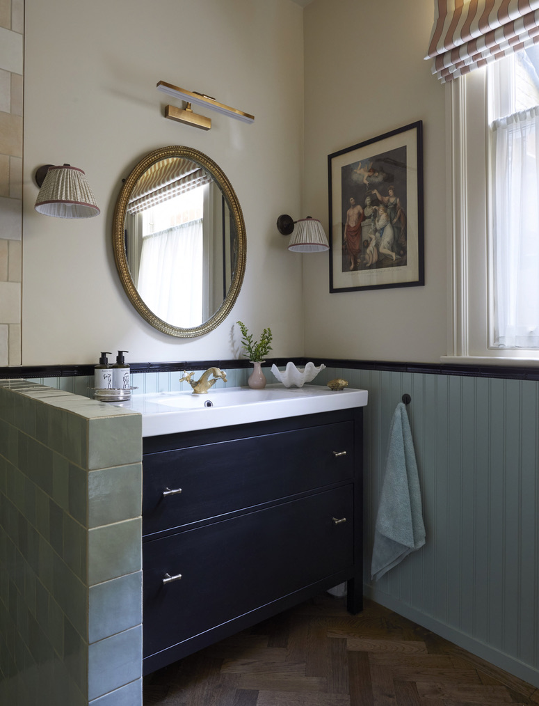a statement bathroom vanity pictured in dark colour with the wall adorned with paintings and lights and a towel