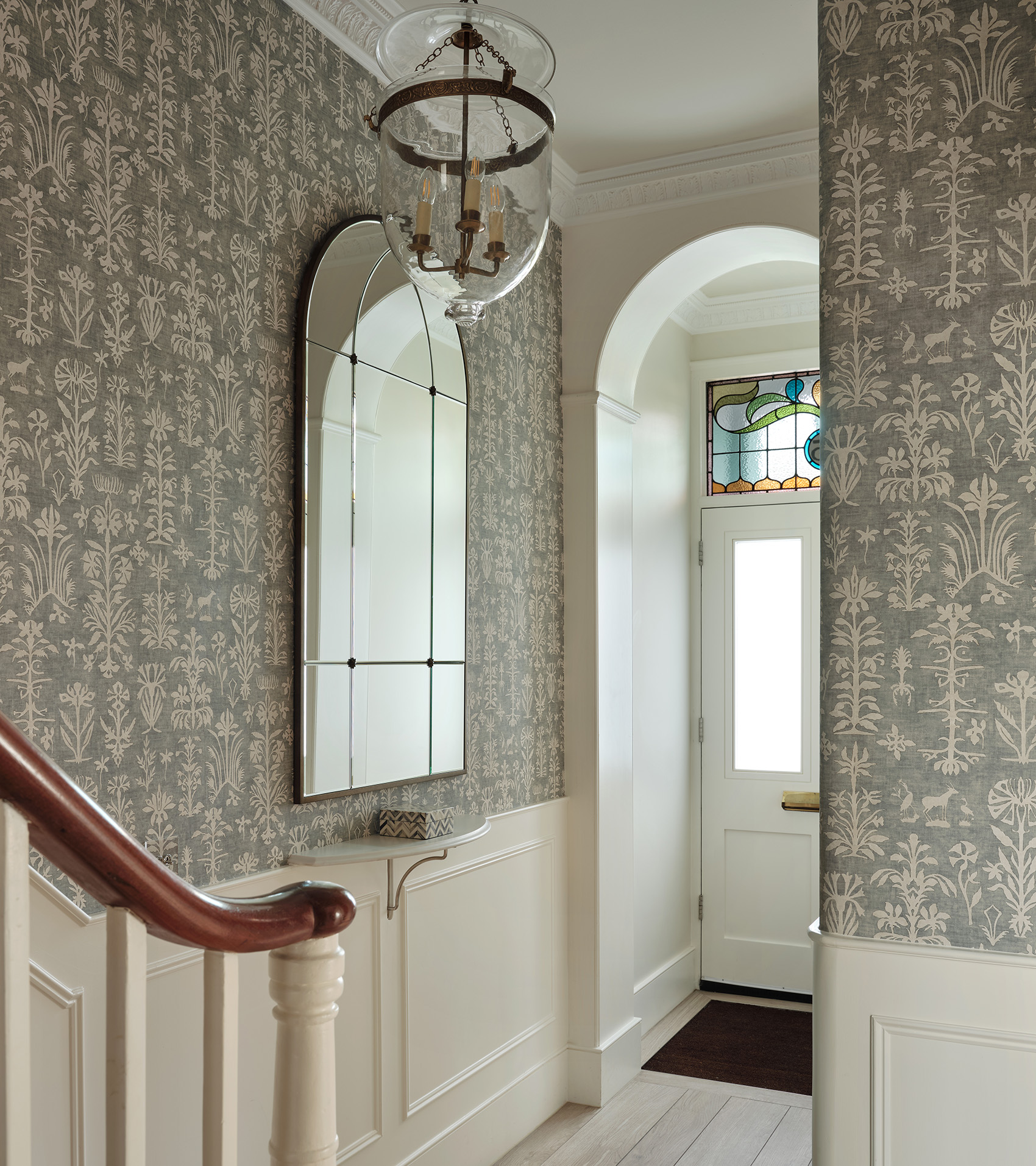 hallway with large arched mirror and grey botanical wallpaper