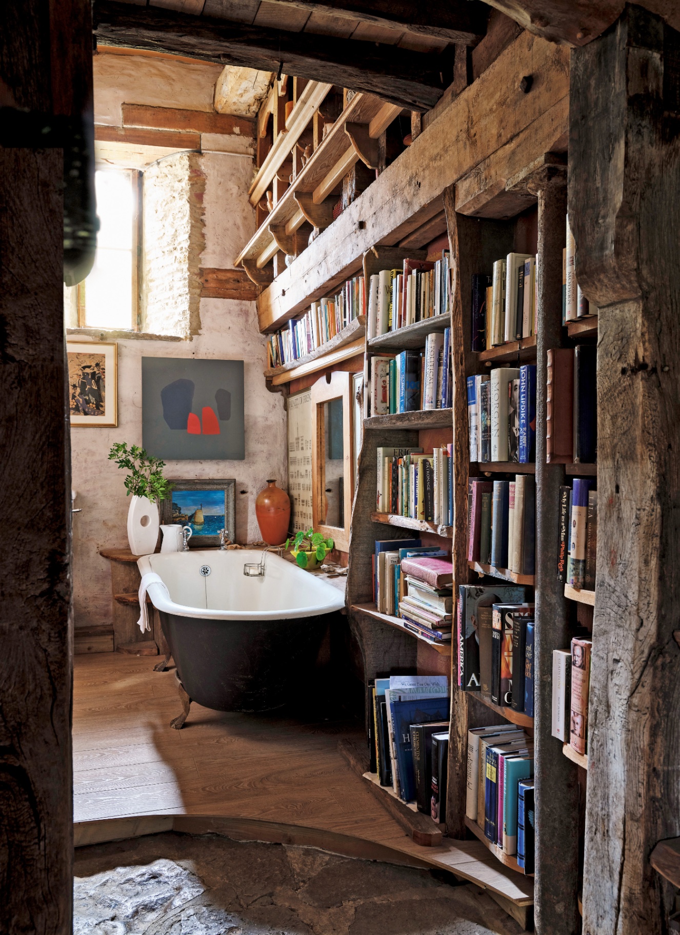 a bathroom with twalls covered in book displays, a black freestanding bath and wooden flooring