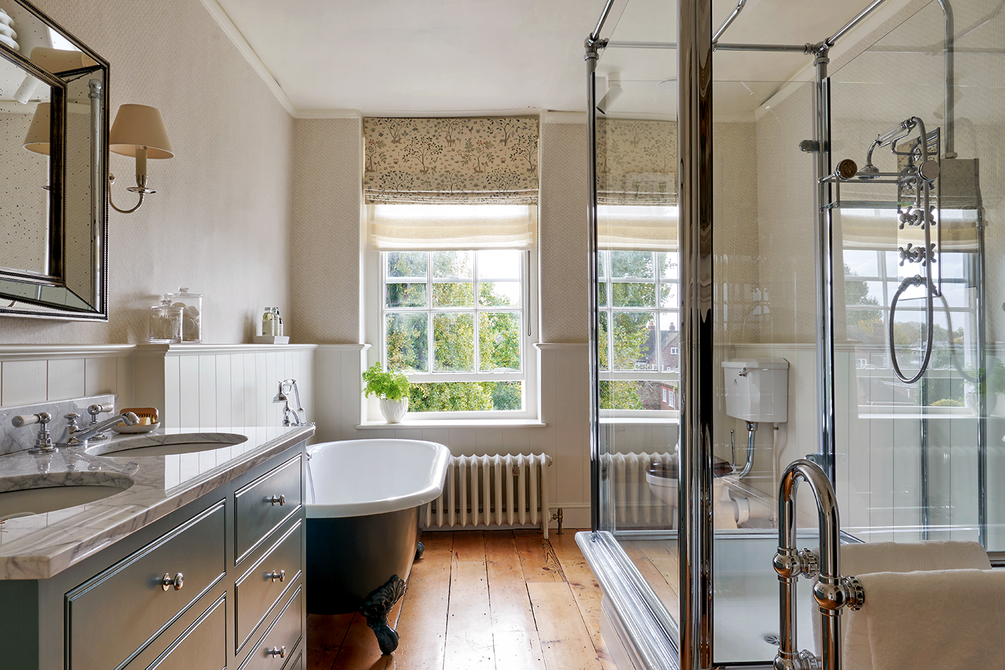 A large bathroom with upper half of walls painted in neutral and lower half with tongue-and-groove panelling. A double vanity unit and freestanding tub sit to the left and a built-in glass shower to the right