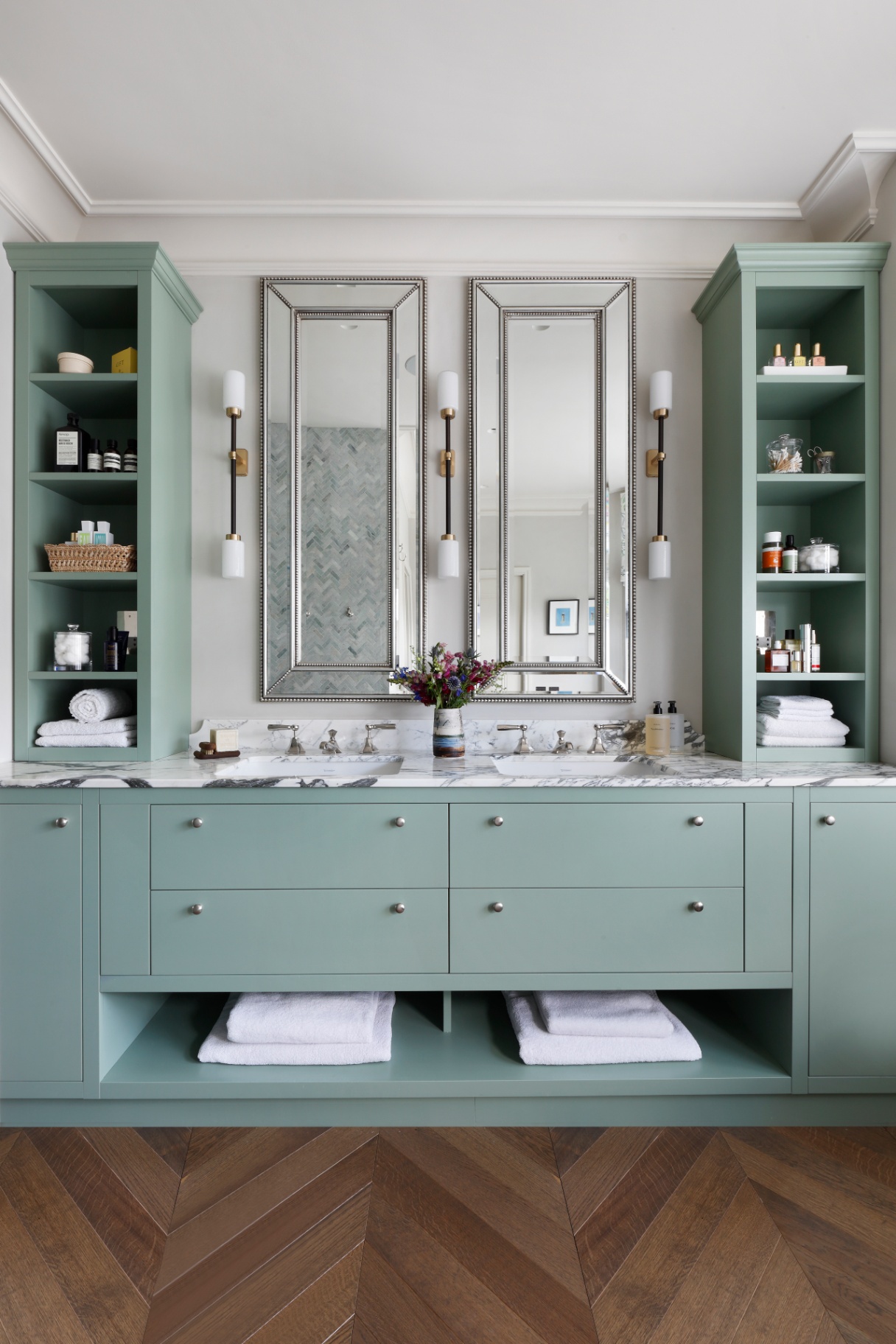 a master en suite pictured with a large double vanity in duck egg blue colour on the side are wall lights and shelves filled with bathroom accessories