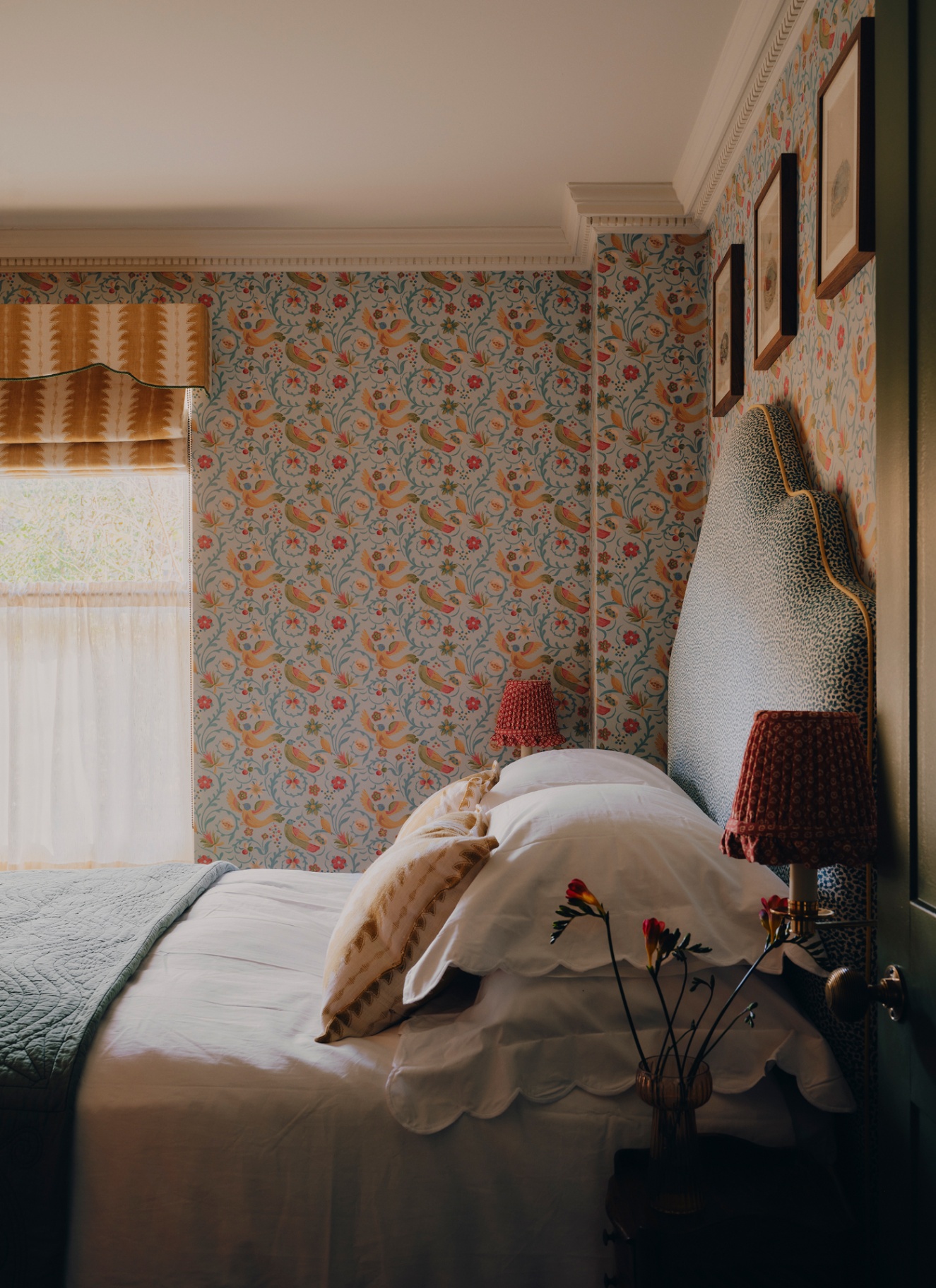 a bedroom with a bed with white bedding and a large scalloped headboard and floral wallpaper