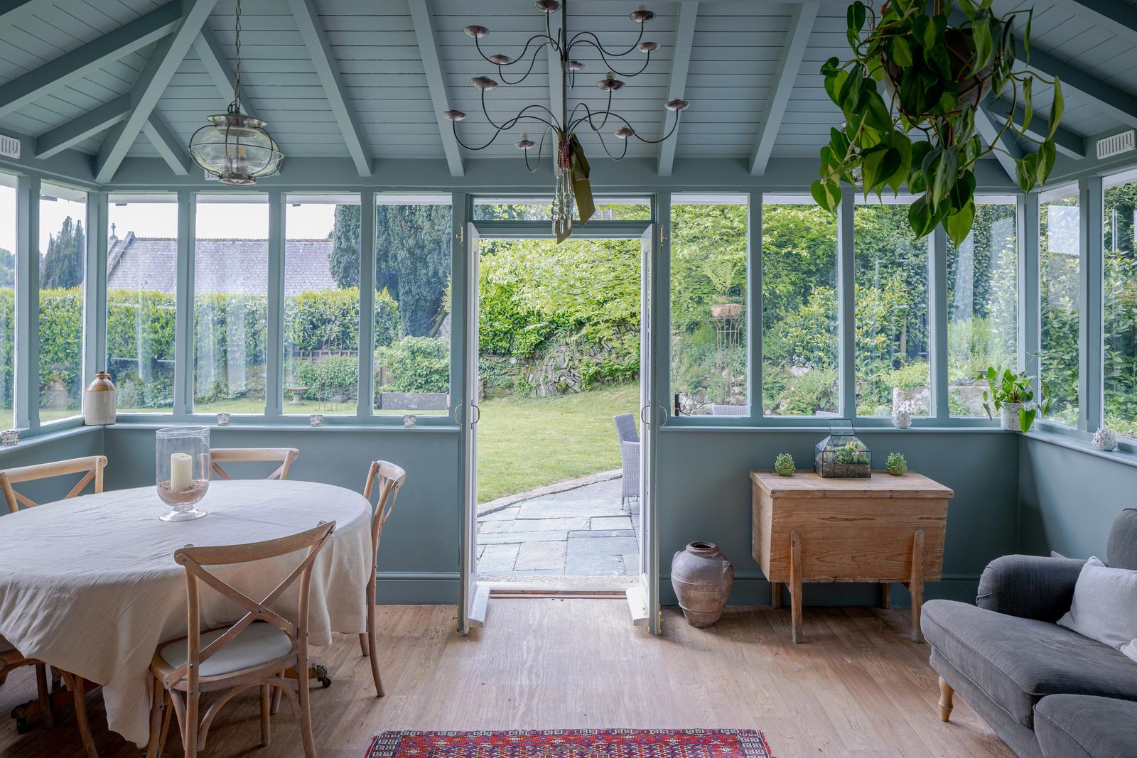 a conservatory with pale blue colour drenched ceiling and walls, a candle chandelier, a round wooden table with a white cloth and wooden floors