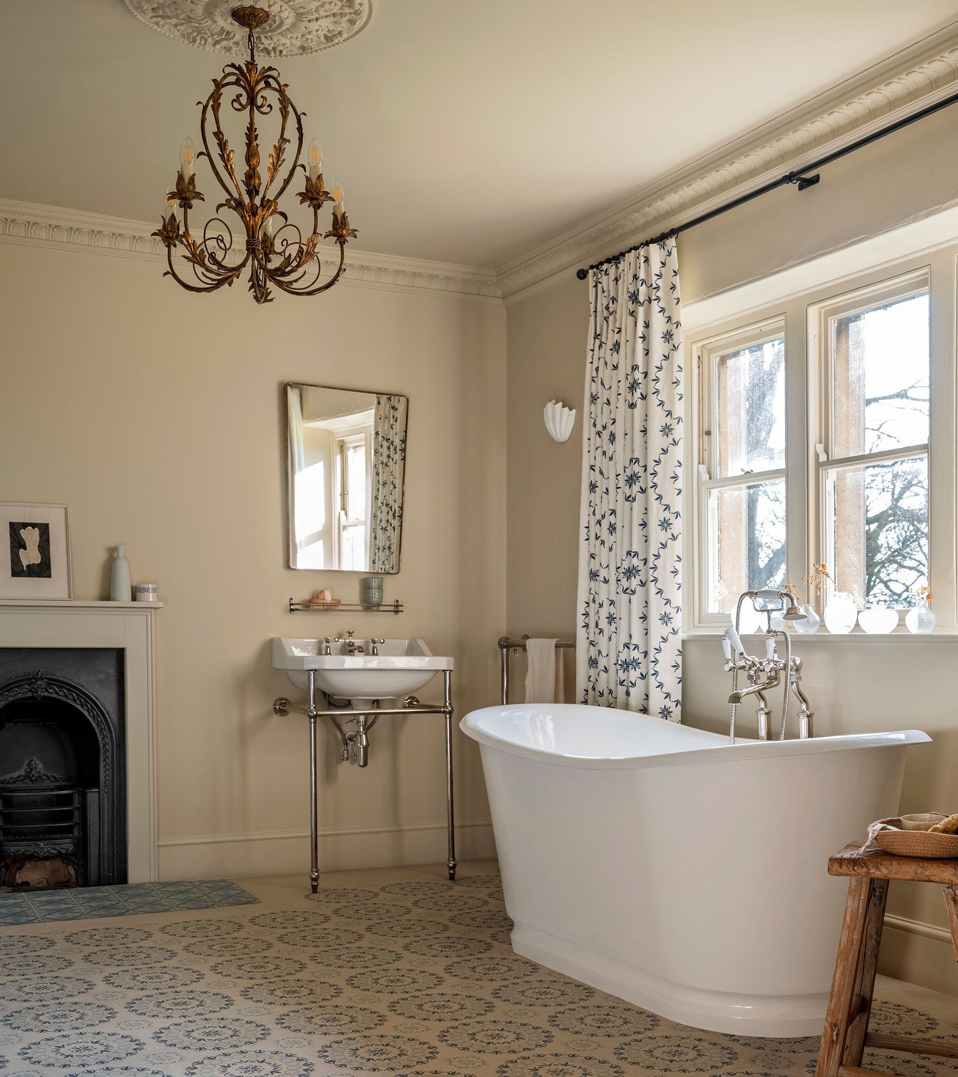 ca pietra bathroom with chandelier, white roll top bath, blue and white curtains, a victorian wash basin with a rectangular mirrow above it, a fireplace