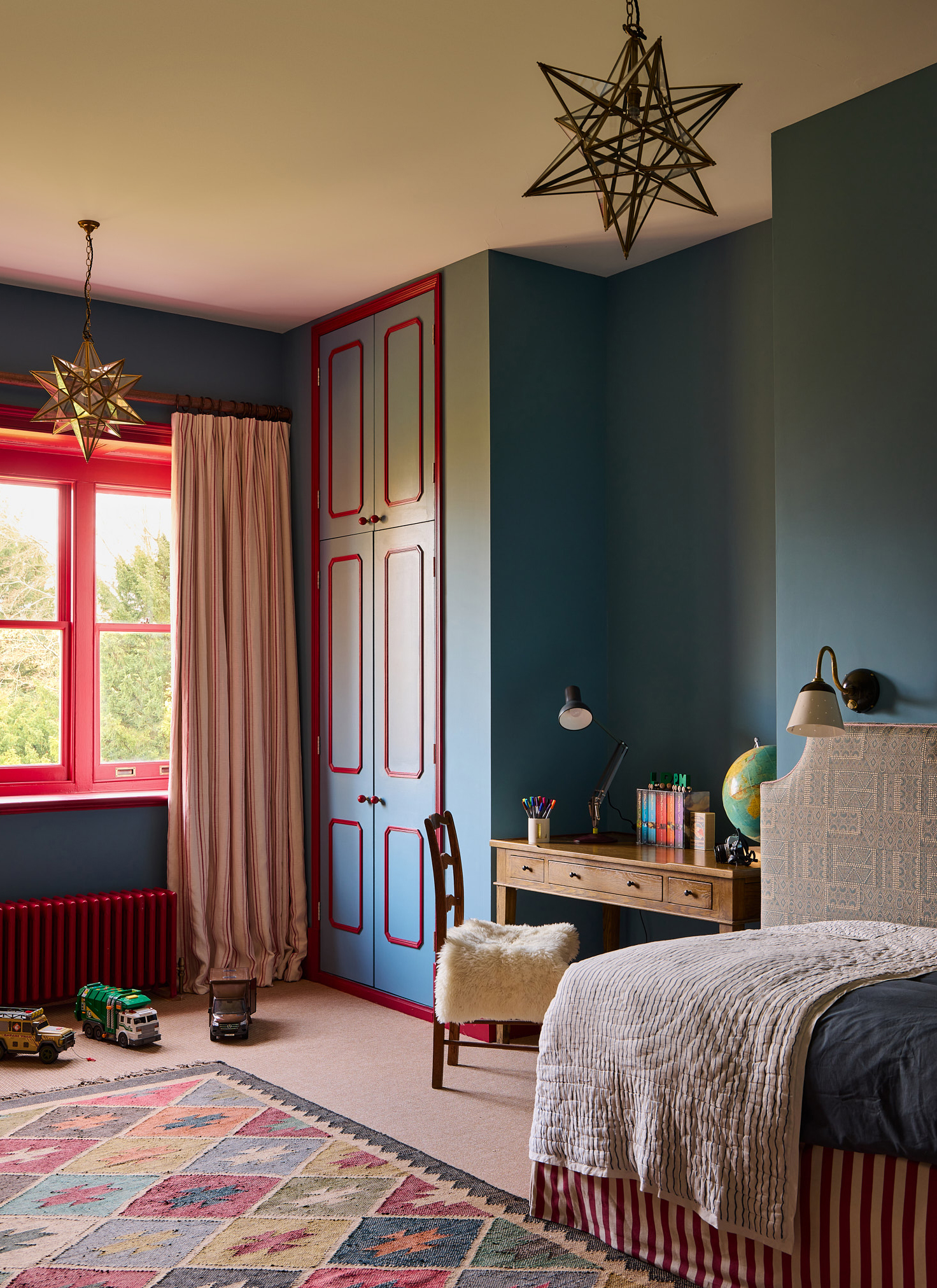 a childrens bedroom with dark blue walls, two star pendants on the ceiling and a multicoloured geometric rug