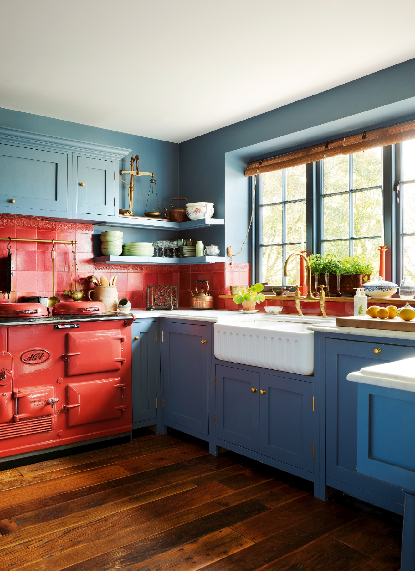 a kitchen with wooden floors, a bright red range cooker, red tiles and bright blue cabinetry and walls
