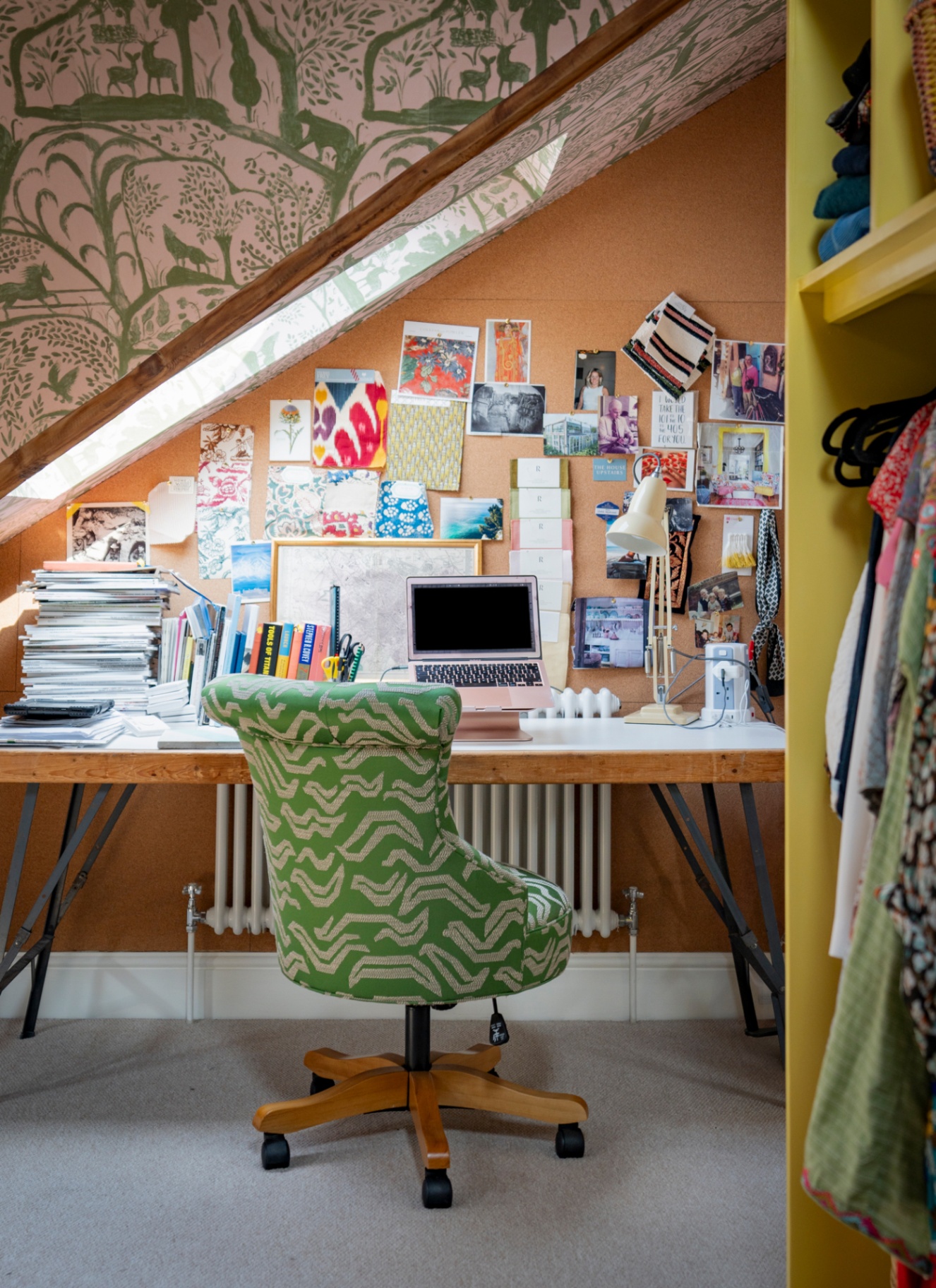 ttic home office setup under sloped eaves with a custom floating timber desk, green patterned wallpaper, and a green upholstered swivel desk chair